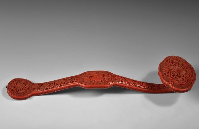 A CARVED CINNABAR LACQUER SCEPTER: A finely carved Qing dynasty cinnabar lacquer scepter with patterns of blooming peony, double fish, and five bats, signifying double happiness, prosperities, and good fortune. The piece is completed w
