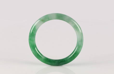 A Mottled Green Jadeite Bangle: 天然翡翠手鐲 Of elegant circular form, the bangle well-polished and carved from a single section of jadeite of bright translucent green tone, subtly mottled with li