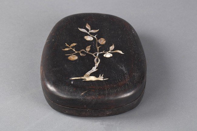 A CARVED INKSTONE WITH COVER: Of tapered ovoid shaped outline with rounded corners, the top carved with a dragon amid swirling clouds. A persimmon tree featured on the outside case, made from abalone shells. Dimension:H: 2 in (5cm