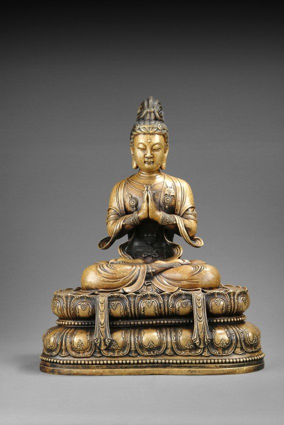 A GILT BRONZE FIGURE OF SEATED GUANYIN: Seated in Dhyanasana on a double lotus base with hands in Namaskara mudra, loose robe draped over shoulder and left open at the chest exposing multiple ornamented necklaces, her expression serene, wit