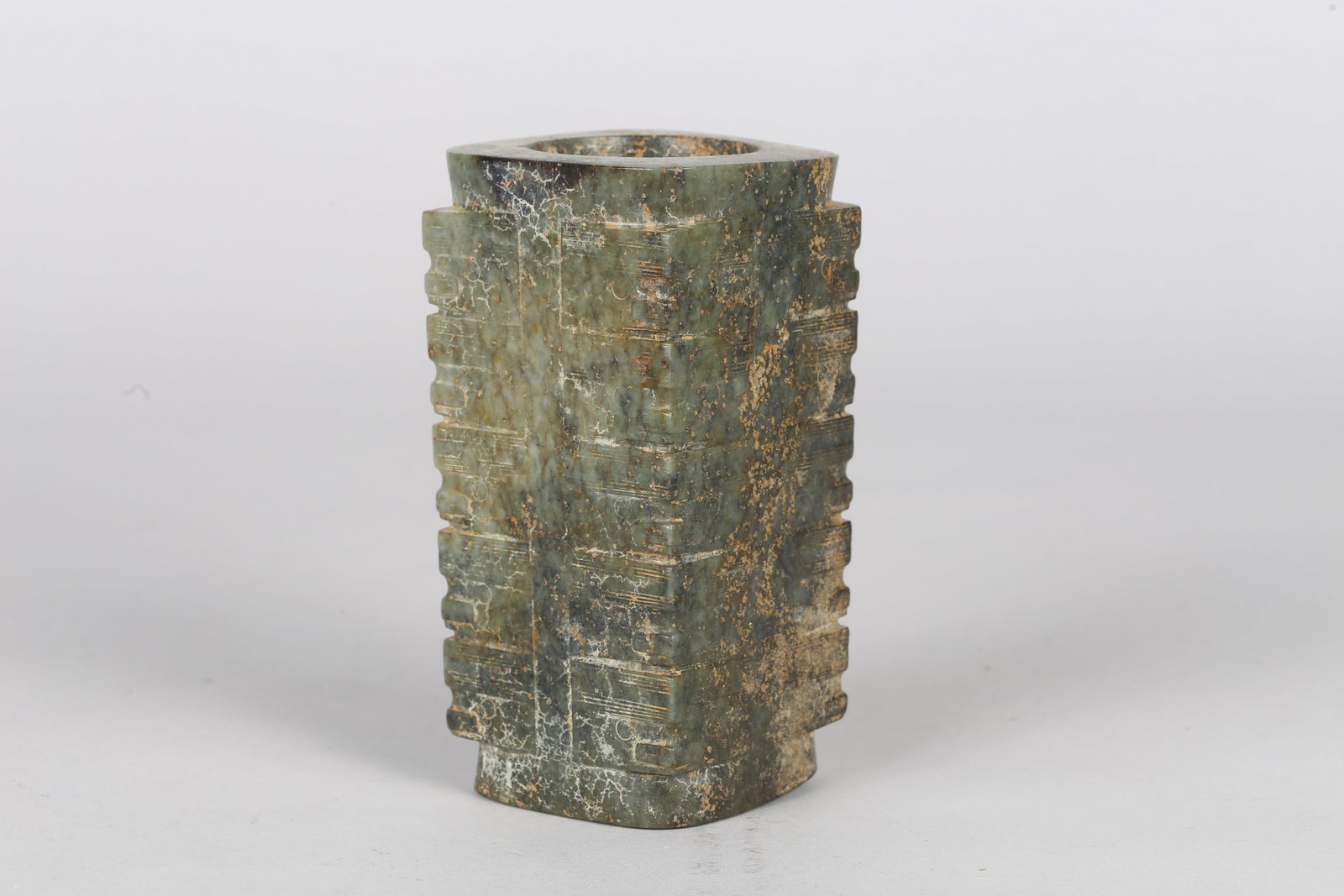 A Large Mottled Green Jade Cong: 良渚 青玉五层琮 Of tall, square-section form with a cylindrical aperture, the exterior carved in five registers with stylized mask motifs, the stone of varieg