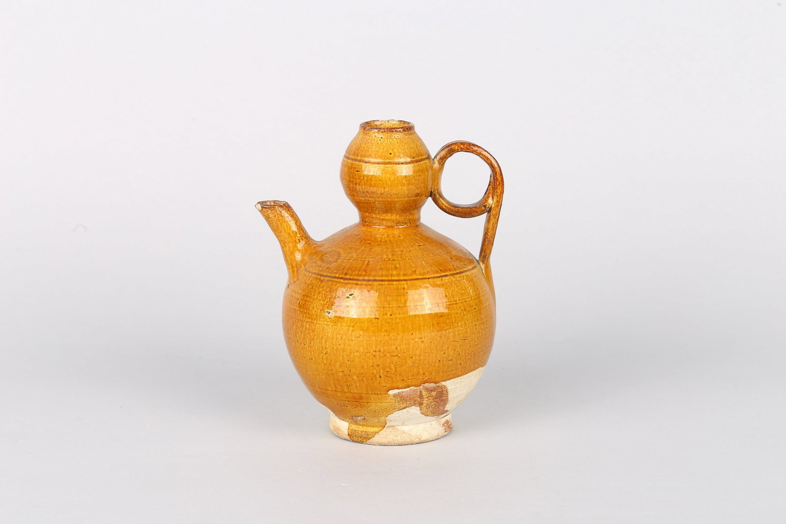 A Chinese Yellow Glazed Pottery Ewer: 遼 黃釉葫蘆式執壺 The globular body rising from a short foot to a waisted neck surmounted by a small bulbous mouth, set with a loop handle opposite a