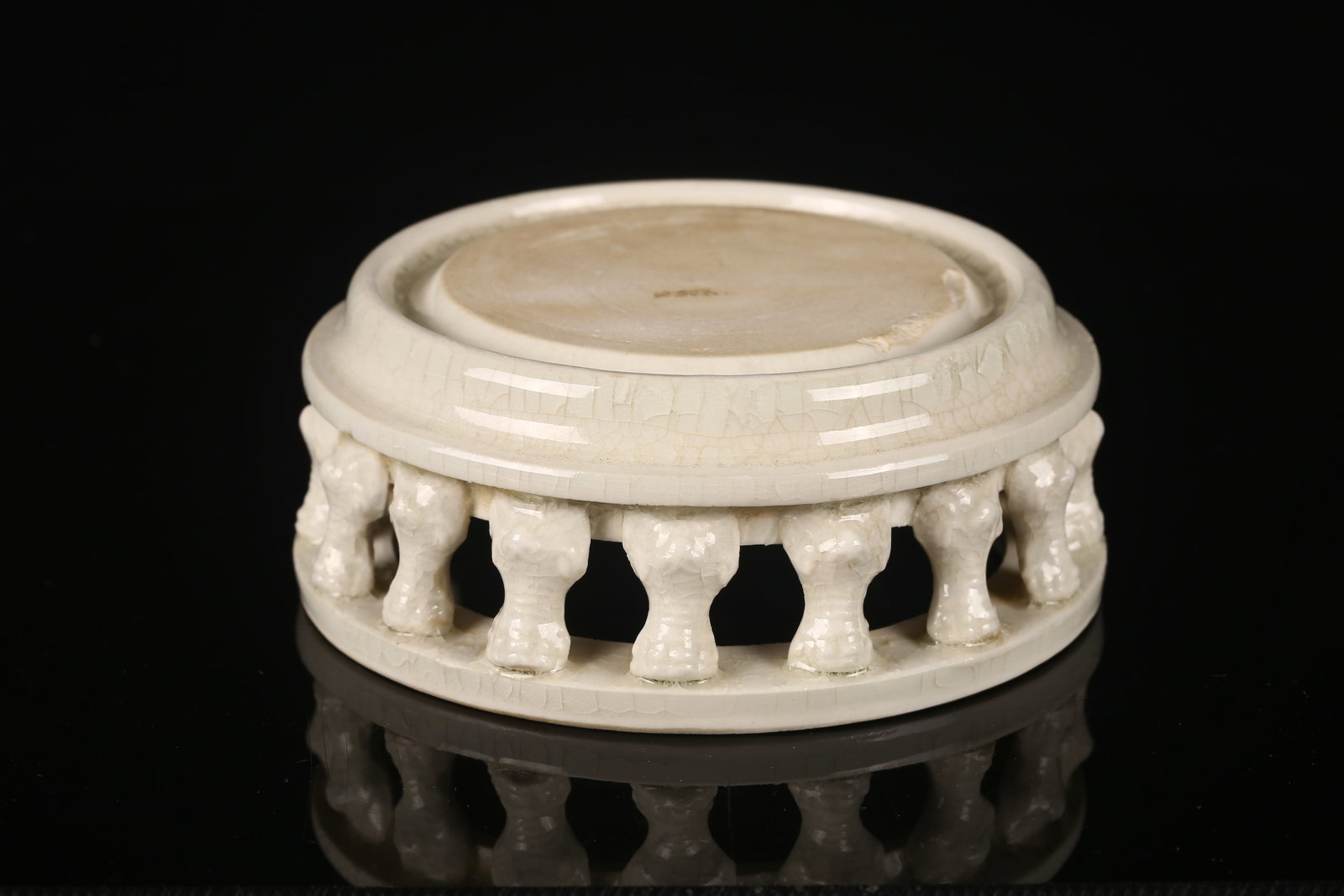 A White Glazed Ink Stone: 白瓷硯台 Of circular form with a shallow recessed well, raised on a reticulated ring of stylized animal-form supports, the sides encircled by a narrow band. Covered overall in