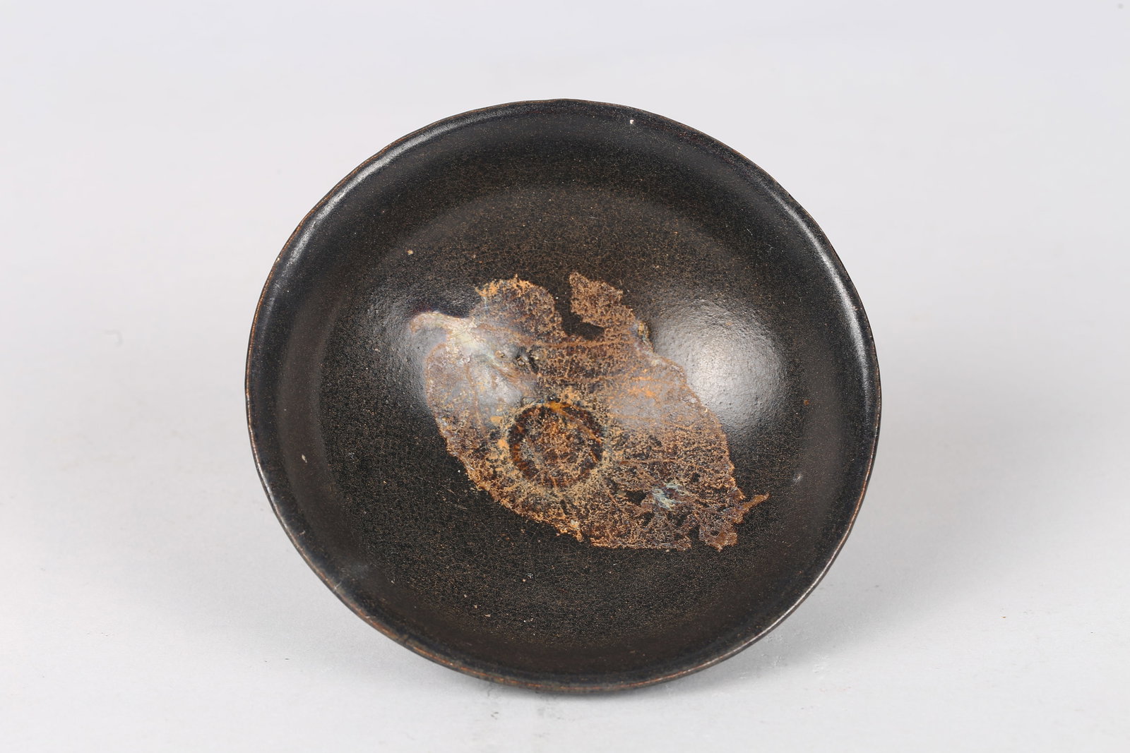 A Jizhou 'Tea-Leaf-Pattern' Tea Bowl: 吉州窯黑釉木葉碗 Of shallow conical form with slightly flared rim, covered in a lustrous dark glaze, the interior centered with a naturalistic leaf