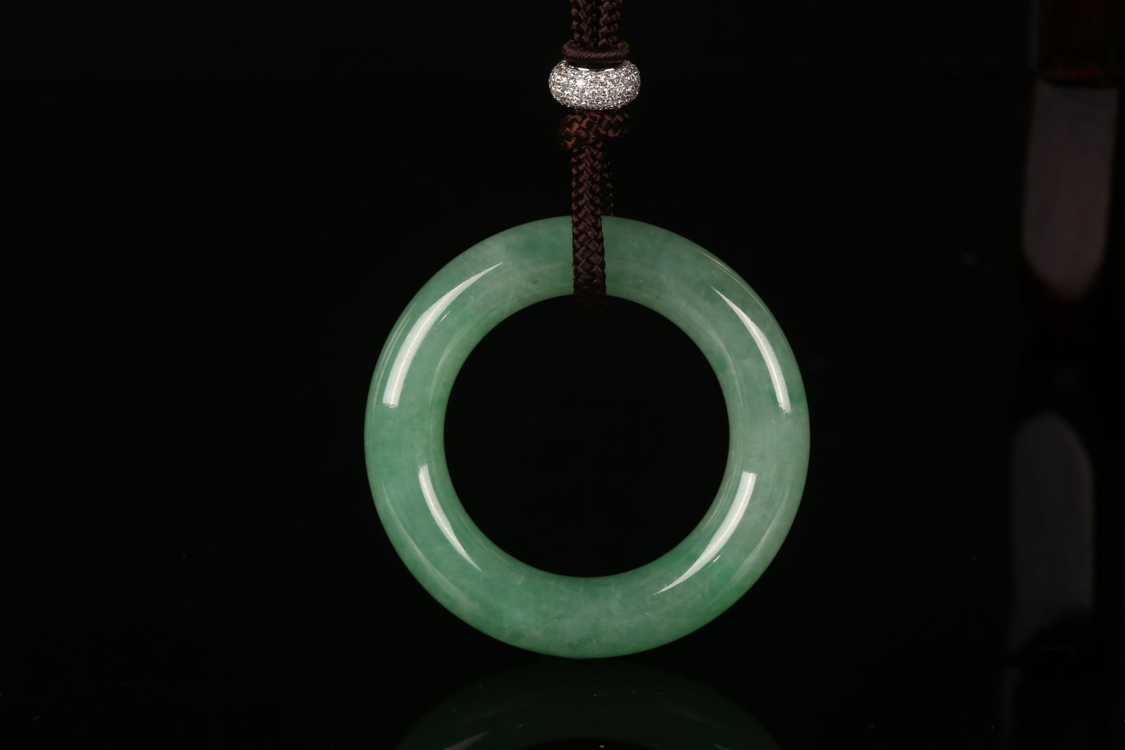 Natural Jadeite Disc Pendant with Diamond and 18K White Gold Mount: 天然翡翠鑽石平安扣 Of circular form, the jadeite disc pendant of high translucency, measuring 52.81 x 33.83 x 9.94 mm, set with a diamond-set 18K 