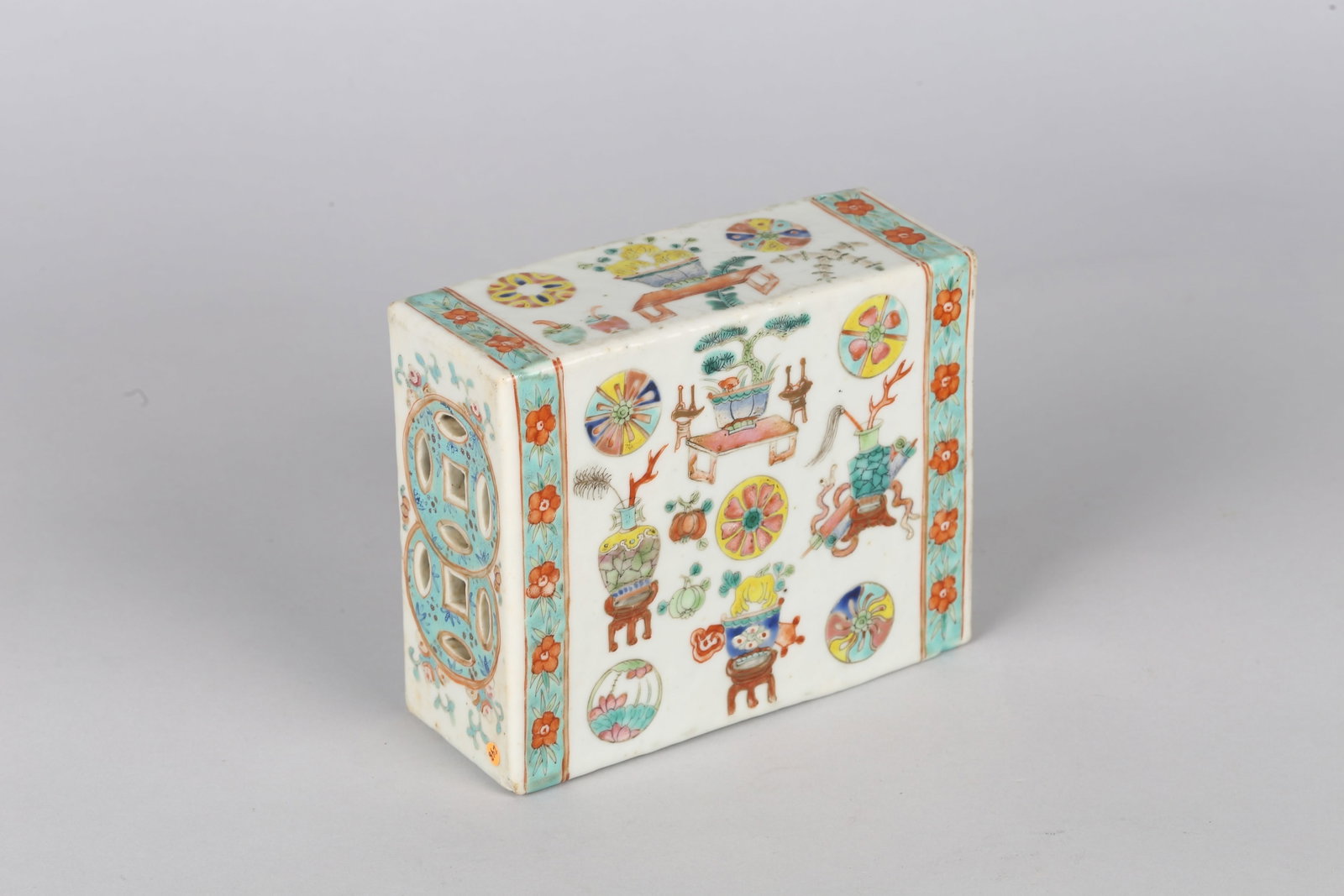 A Chinese Famille Rose Pillow: 清 粉彩博古皮球紋枕 Of rectangular brick form, one end pierced, decorated with scenes of flowering vases and roundels. Qing Dynasty period. Height