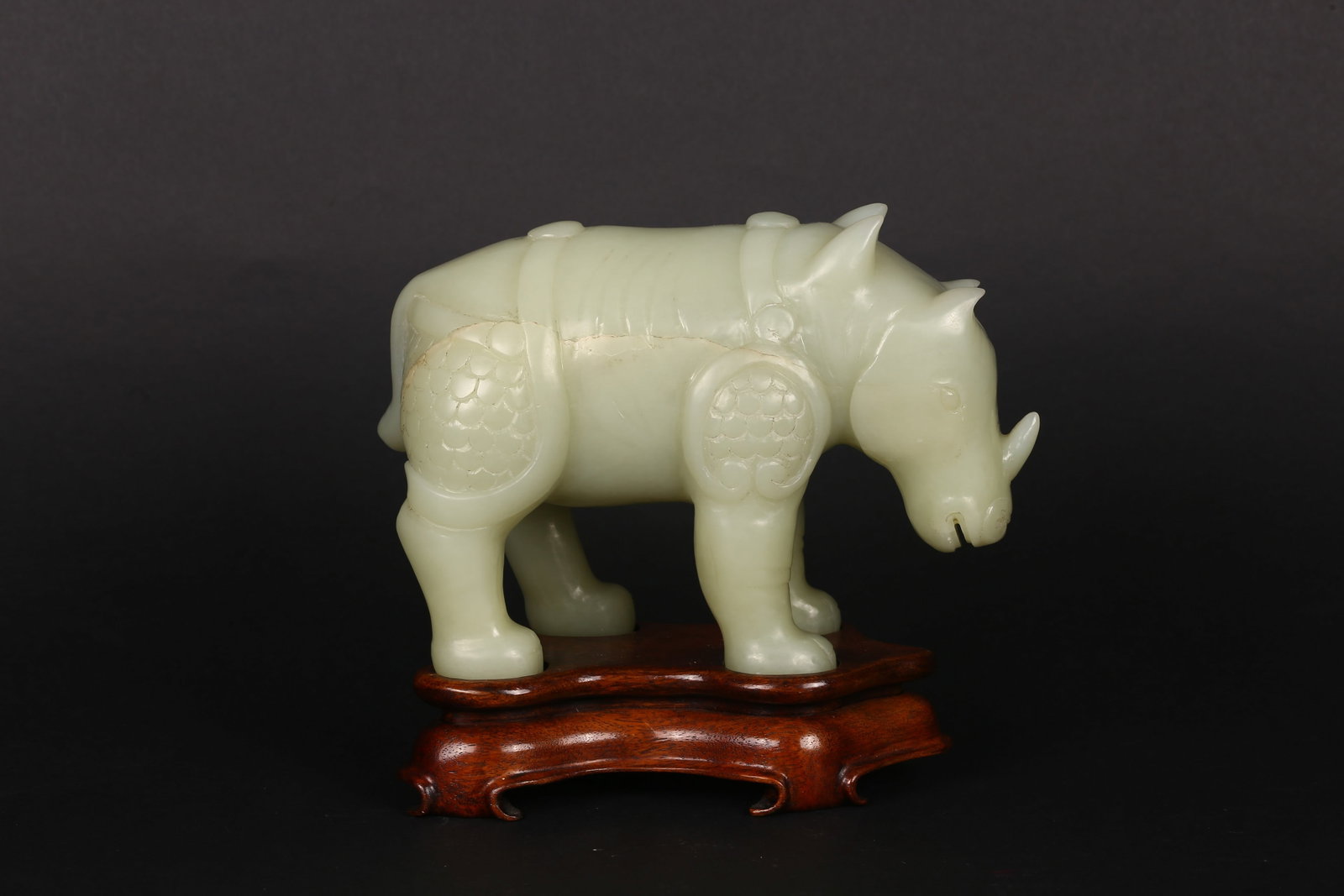 A Celadon Jade Carved Figure of Rhinoceros: 青白玉雕兕 Carved in the round from a pale celadon stone of even tone, the animal shown standing foursquare with head lowered, its sturdy body modeled with gentle