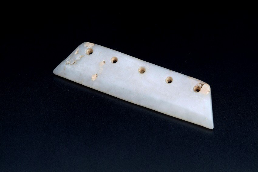 A CHINESE JADE AXE SHAPED ORNAMENT: This jade ornament is of axe shape, with drilled holes around one edge. Warring States period. Dimension: L: 3 3/8 in (8.7 cm)