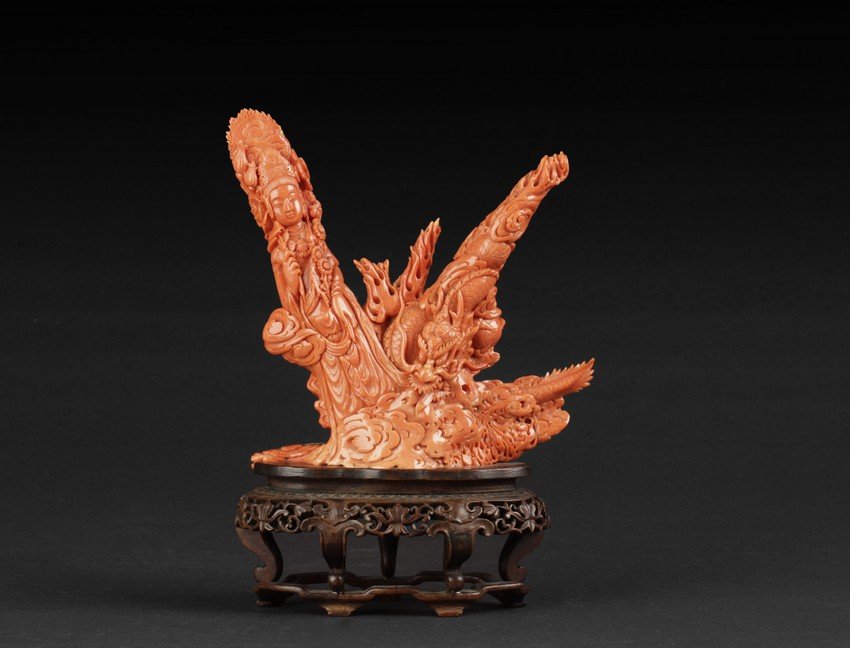 A carved coral 'Guanyin and Dragon' figural group: Leaning sideways, the Guanyin is holding lingzhi in one hand, flowers in the other, dressed in flowing robes and ornate crown, she flies amidst clouds next to a fierce dragon, the body and claws mostl