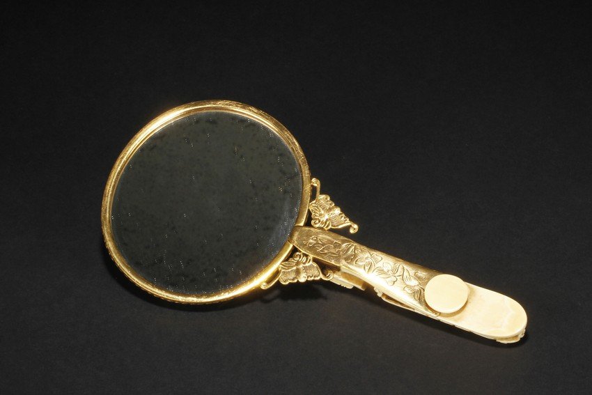 A GILT SILVER IVORY HANDLE HAND MIRROR: The mirror of perfect round form, framed with gilt silver, attached to a gilt silver and ivory handle incised with flowers and leaves patterns, enforced by two flying gilt-silver bats, the reverse sid