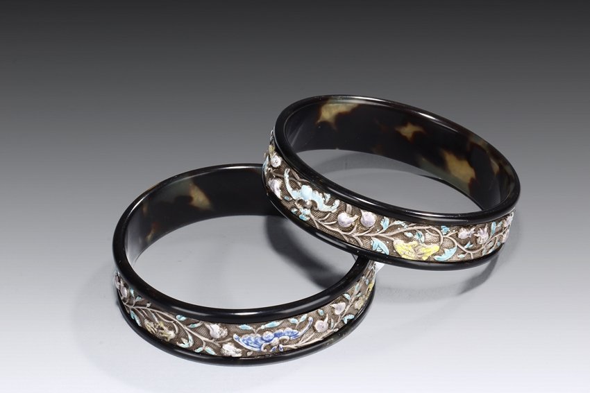 A PAIR OF SILVER GILT ENAMELED TORTOISESHELL BANGLES: The round bangles made from tortoiseshell, inset with a gilt silver band depicting bats, flowers, tendrils, and leaves, with teal, blue, and yellow enamel on the surface. Late Qing Dynasty period. D: 