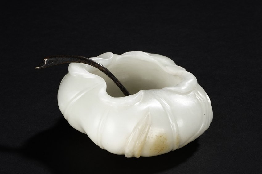 A CARVED WHITE JADE "LOTUS LEAF" WASHER: The washer with lotus leaf folding upwards design, the stems and root lightly carved, the white jade of smooth white with slight translucency and russet. Qing Dynasty period. L: 3 1/2 in (8.9 cm) H: 1