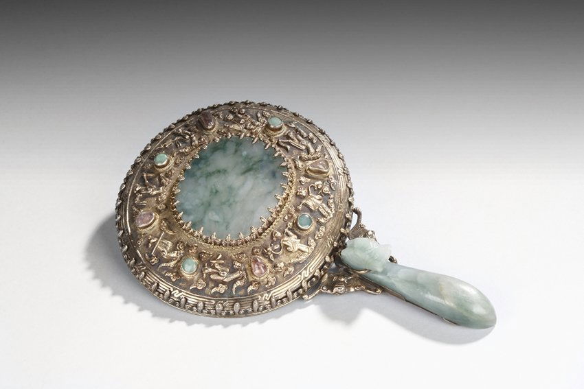 A JADEITE AND GOLD-SILVER MOUNTED MIRROR WITH GEMS INSE: This rounded hand-mirror is delicately decorated in medium relief with various human figures and gems inset. It is inlaid to the back with a jadeite plaque and small pink . The handle is formed of a j