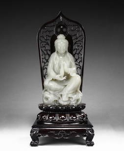 A LARGE WHITE JADE 'GUANYIN' WITH ZITAN BASE: The Guanyin is shown seated on a stand, with one feet resting upon a lotus flower and both hands holding a vase. She wears a gracefully loose robe exposing the ornate bead necklace on chest and her fa