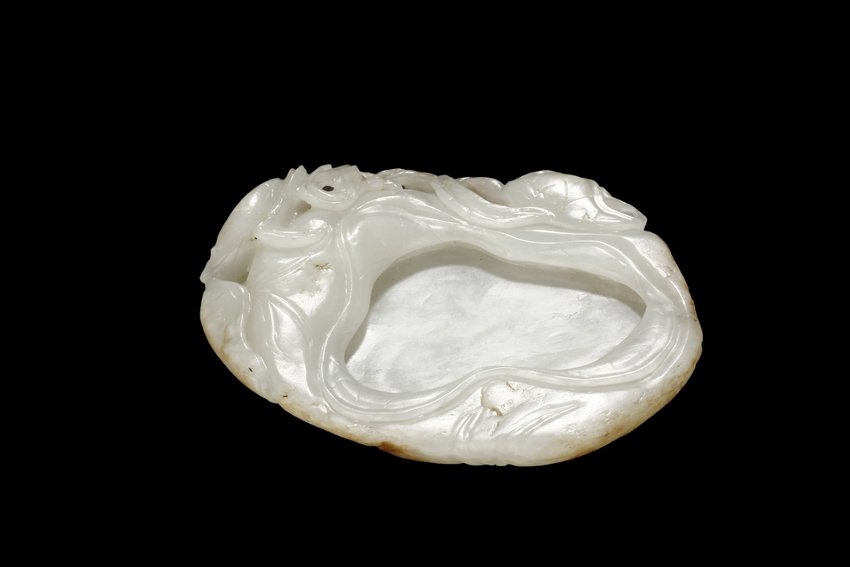 A CARVED WHITE JADE "LOTUS" WASHER: Of compressed floral form, the washer in the shape of a large lotus leaf with bent corners, the side with lotus bulb ready to blossom and vines, the stone of white with mottled and translucent interio