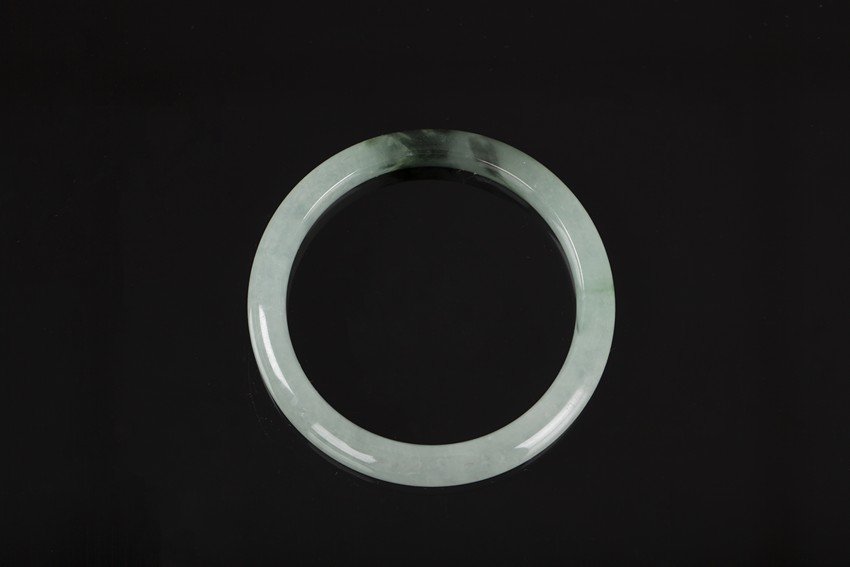 A JADE BANGLE: The jade bangle is of circular outline with a central aperture, mostly translucent with a patch of dark green. H: 3/8 in (1 cm) Outer D: 2 3/4 in (7 cm)