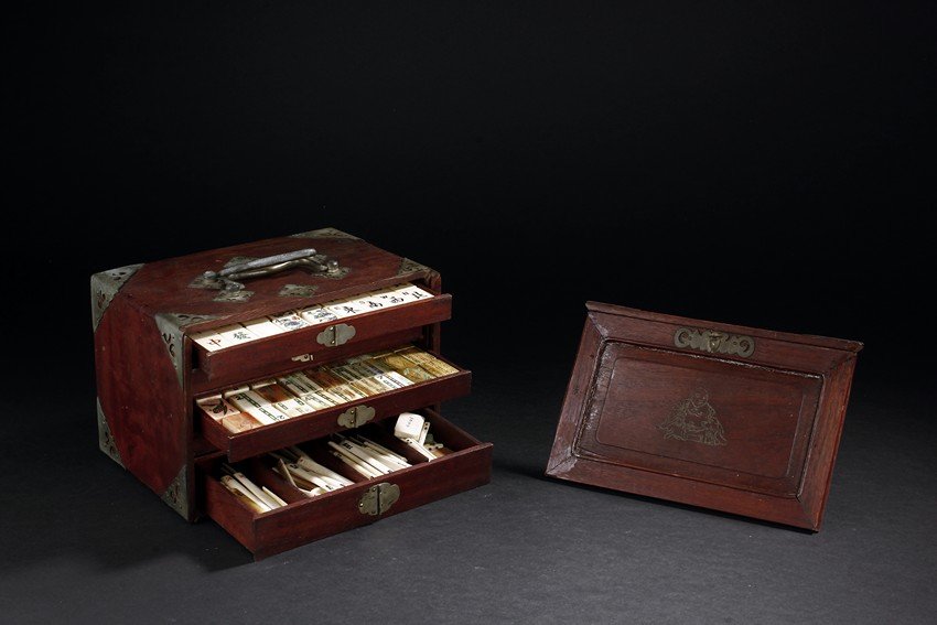 A SET OF BONE & BAMBOO MAHJONG & HARDWOOD CABINET: The cabinet containing three drawers, with the bottom one divided into three compartments, each enclosing a set of mahjong and dominoes. Each piece is polychromed. Box: H: 6 3/8 in (16.2 cm) L: 9 1/2 