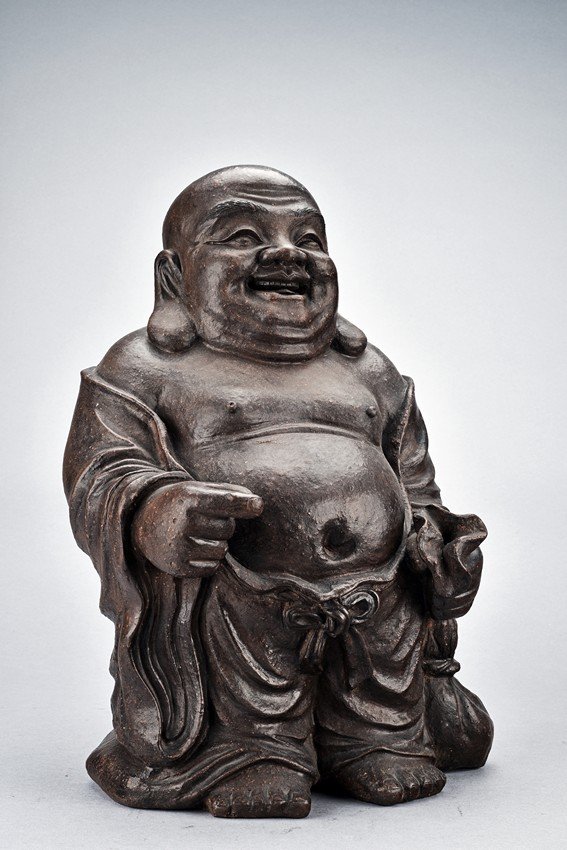 A YIXING ZISHA FIGURE OF BUDAI: The figure is shown wearing long flowing robe, the large belly exposed, left hand dragging a bag, the face with laughing expression flanked by two large and pendulous earlobes. Qing Dynasty period. He