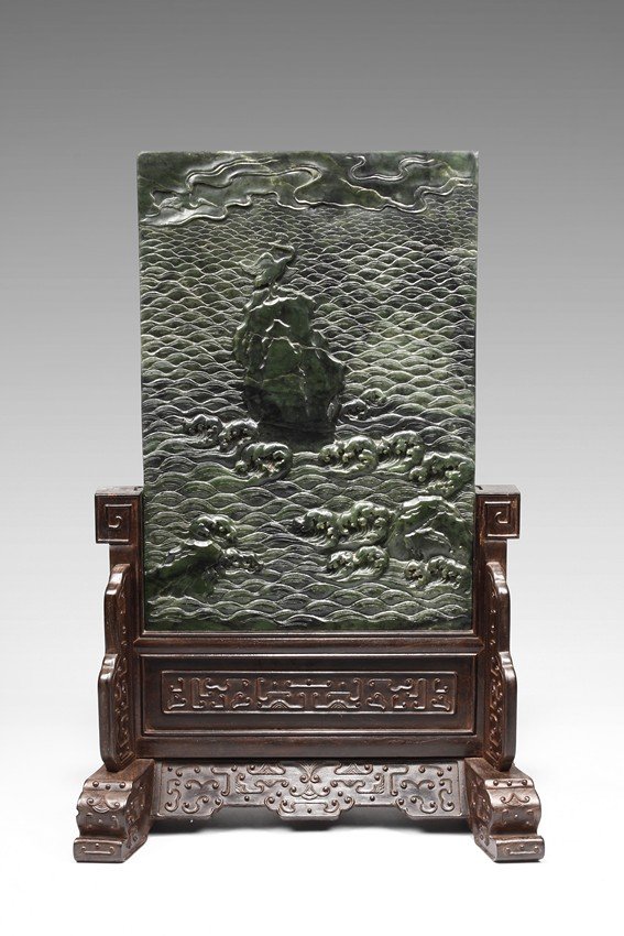 A SPINACH JADE 'CRANE' RECTANGULAR TABLE SCREEN: The plaque is delicately carved in relief to depict a sea cliff landscape. It is detailed with a crane standing on top of a cliff with one leg lifting up, its head turned back to view the sky where an
