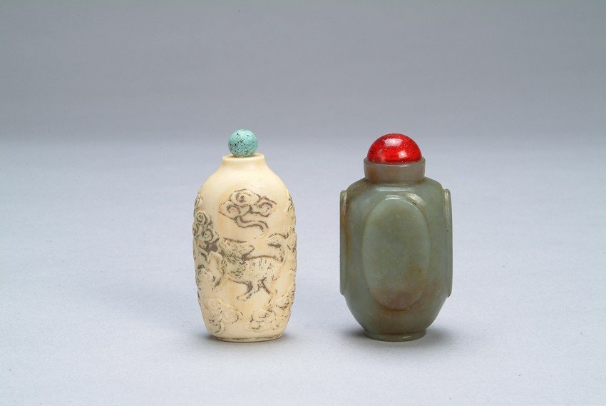 A PAIR OF CHINESE SNUFF BOTTLES: Two intricately made snuff bottles. The first is of cylindrical form, lightly carved with mythical creatures on both sides. The second, a somewhat cylindrical form, is of even celadon green tone with