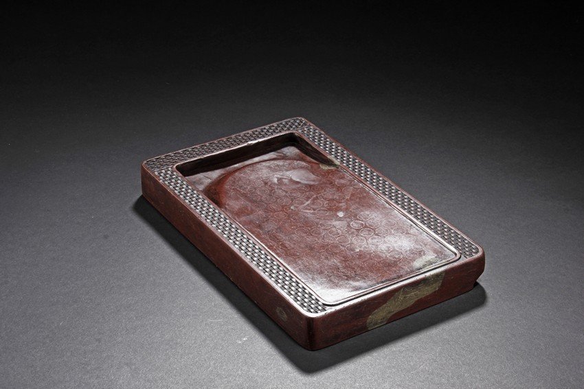 A CHENGNI INK STONE: The ink stone is of deep red-orange color, the edges in chain link pattern, with inkwell on the one side, carved deeply with a curved pattern. Height: 1 in (2.5 cm) Length: 9 1/2 in (24.1 cm) Width: 6