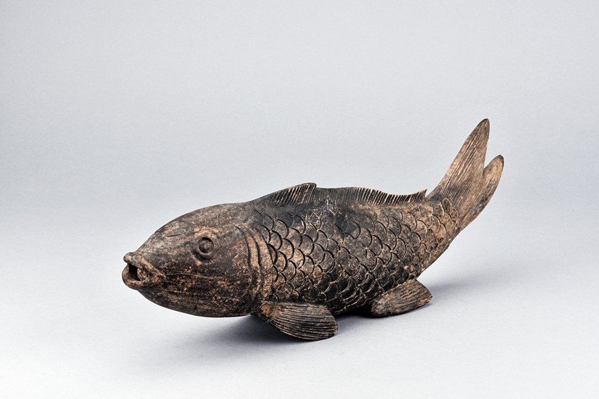 A WOOD CARVED MODEL OF FISH: The wood carving is realistically modelled as a fish flicking its tail slightly upwards, the body finely incised to represent scales. Length: 18 1/2 in (47 cm)