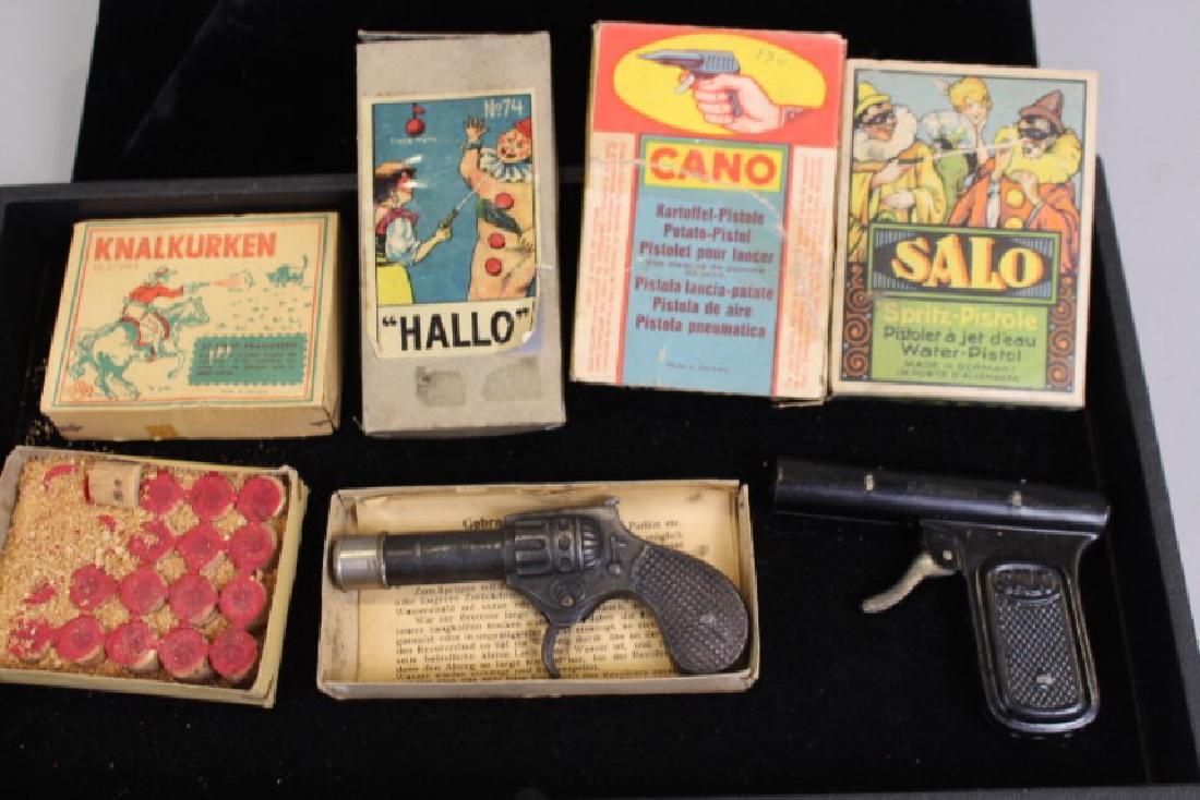 German Squirt Guns & Box Lot of Cork Gun Corks: All in original boxes - unused box of corks; "Hallo" tin pistol style squirt gun with clowns on box lid; "Salo" tin pistol style squirt gun with clowns on box lid; empty box for Cano squirt gun, no gu