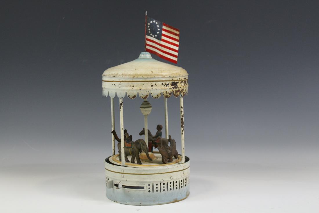 Tin Wind-Up Carousel Ostrich, Elephant, Horse: Painted tin wind-up / clockwork carousel / merry-go-round with horse, elephant, ostrich, and a chariot with riders, 14'' H including American Flag. Working although a slightly sluggish and sometimes n