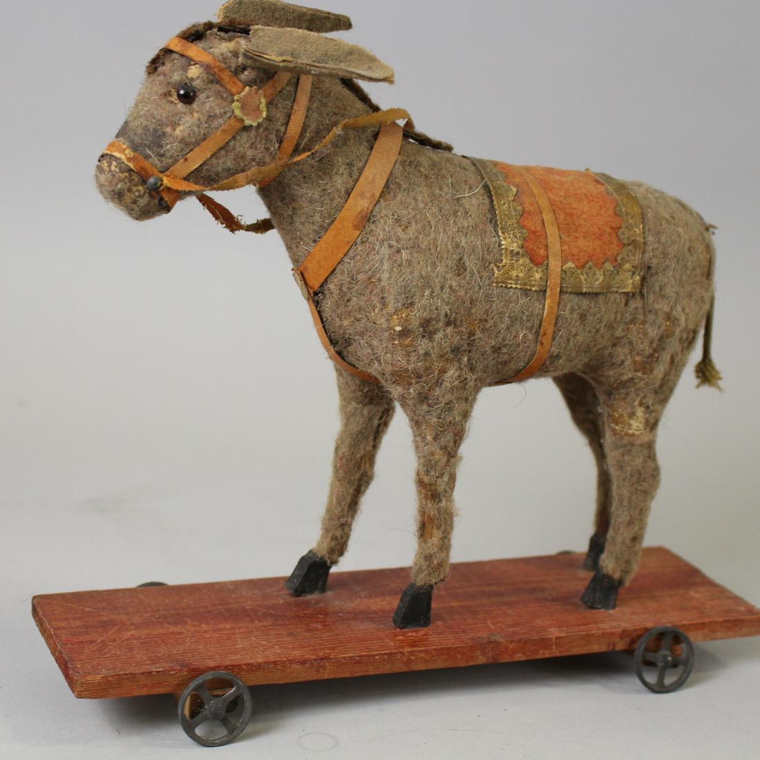 Early 20th C Mohair Covered Donkey Pull-Toy: Late 19th to Early 20th C Mohair Covered Donkey Pull-Toy - glass eyes, complete harness, reins and saddle blanket, mounted to painted red platform, stick legs, spoke metal wheels, 9" H x 10" L. Sporad