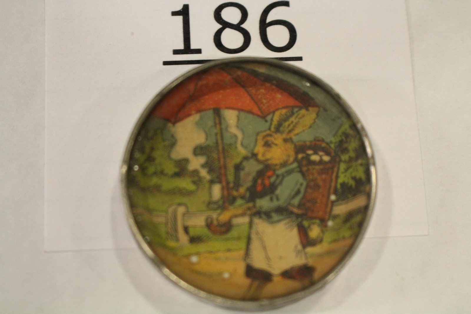 Easter Rabbit Dexterity Game: Dexterity game / handheld puzzle game with image of a Easter rabbit smoking pipe under an umbrella and basket of eggs on his back, metal frame, mirrored back, 1 1/2" W. Good, some minor silver loss to