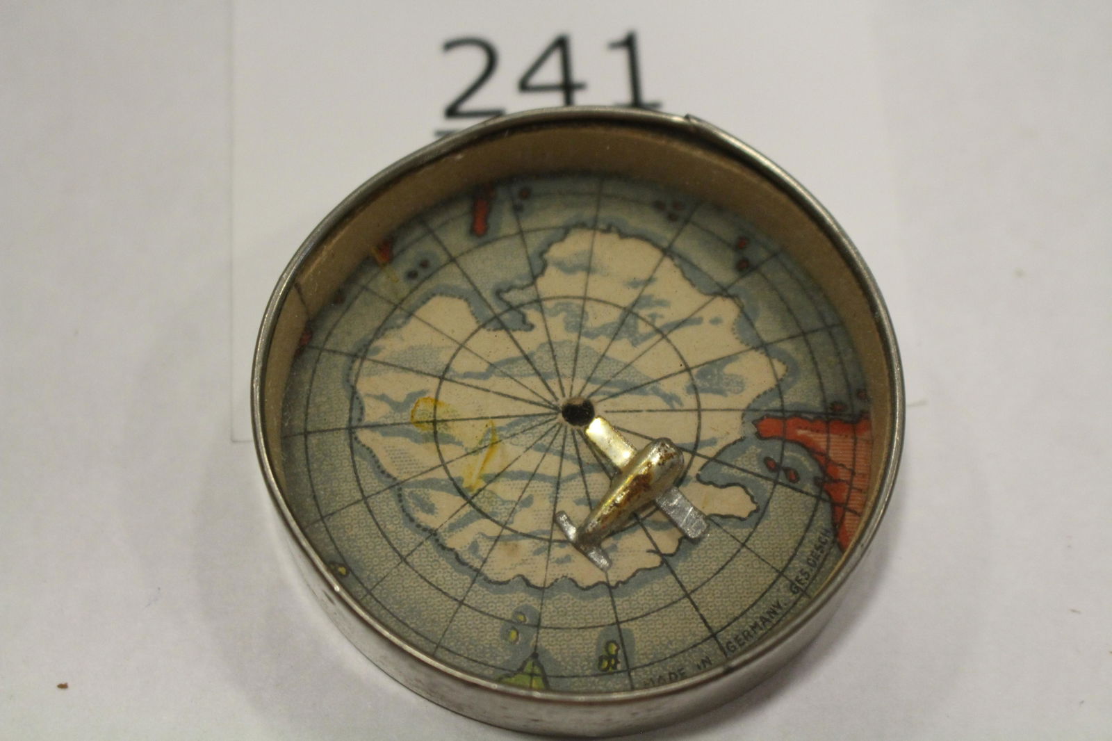Metal Airplane & World Map Dexterity Game: Dexterity game / handheld puzzle game with image of a world map / globe, challenge is to get the metal airplane to land on North / South? Pole, metal frame, mirrored back, 2 1/4" W. Good.
