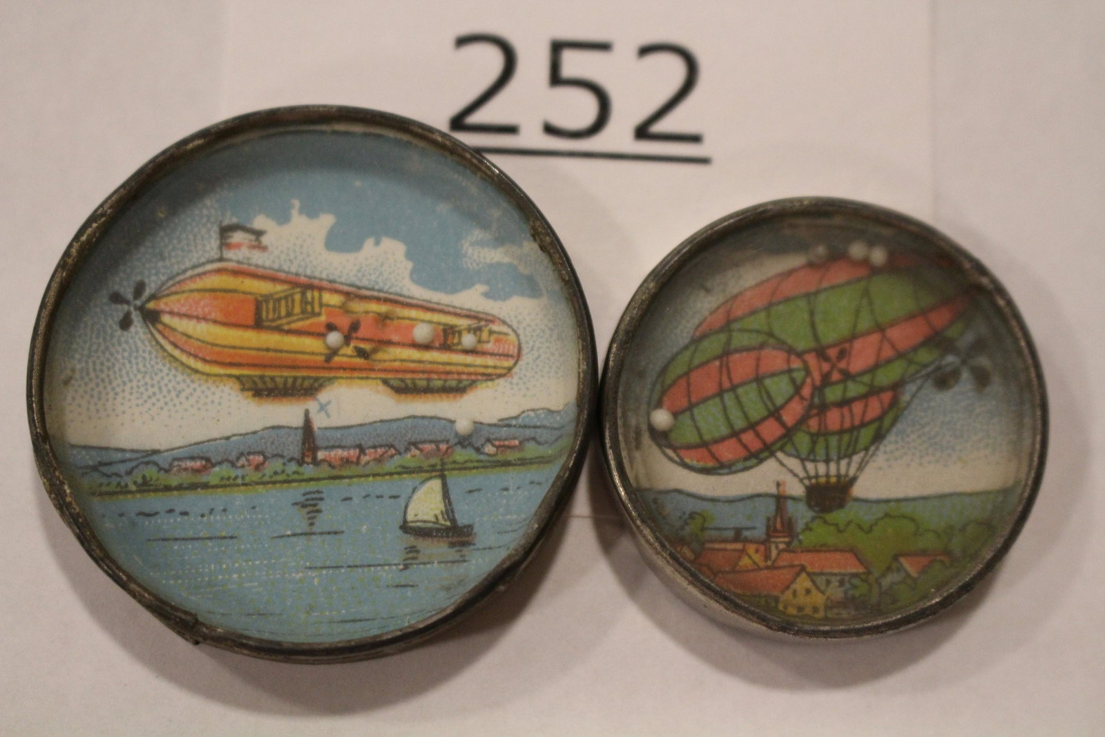 Lot of 2 Blimp / Dirigible / Zeppelin Dexterity Games: Lot of 2 blimp-themed dexterity games / handheld puzzle games with images of a blimp / Zeppelin / dirigible - 1) background of an ocean bay; 2) flying over church and village, both with metal frames, 