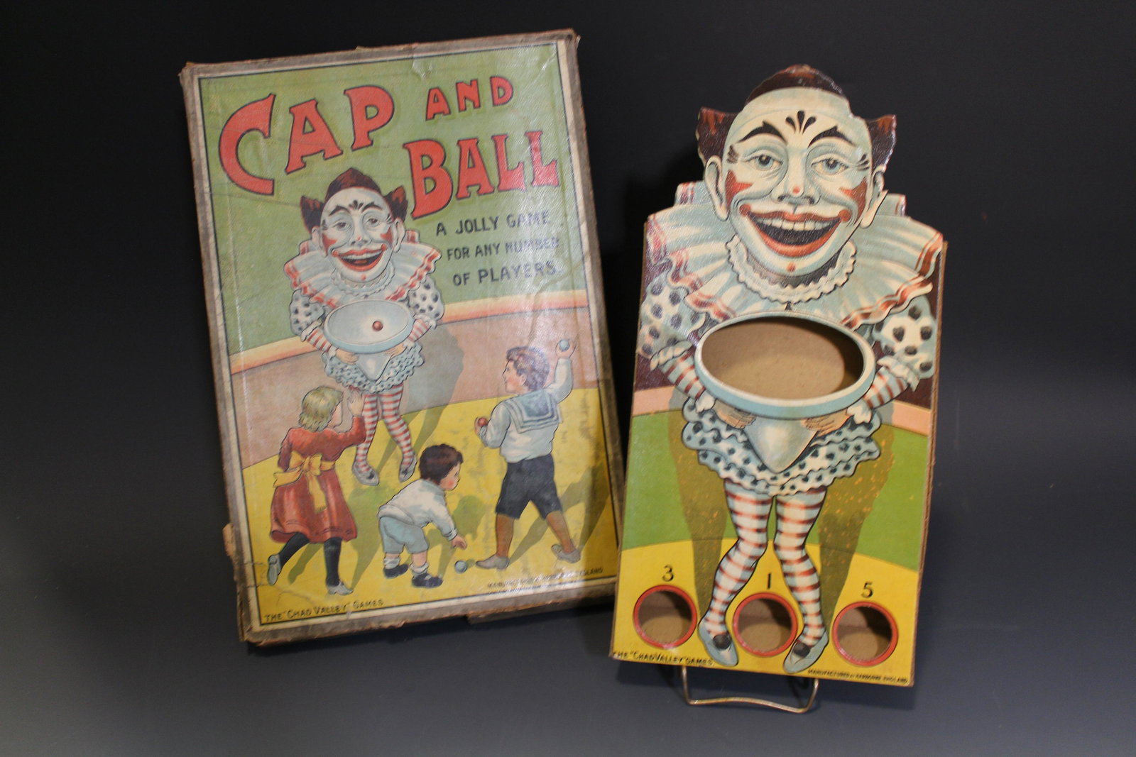 Cap & Ball Target Game - Die Cut Clown: Cap & Ball Target Game - Die Cut Clown, graphic cover and target, cover with Victorian children pitching balls towards clown, scoring game, Mfg. by Chad Valley Works, England, game instructions under