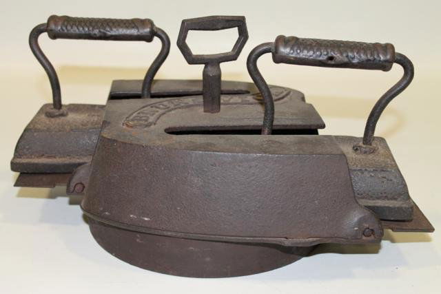 Rare Brunswick Double Flat Irons in Cast Iron Triv: Trivet signed Brunswick, trivet drops into cast iron stove pot opening to heat, double matching irons each marked "7",