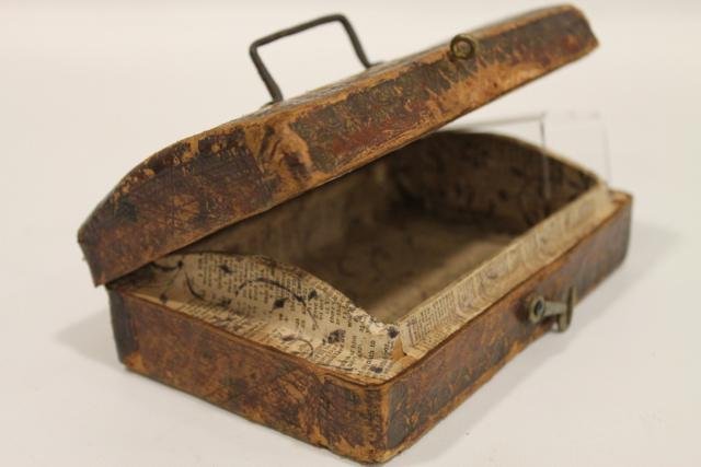Tooled Leather Covered Miniature Box: Early 19th C. leather covered box, hand-forged handle, hook and eye closure, slightly humped lid, lined with old Bible or Biblical quotes paper, 6 3/4" long.
