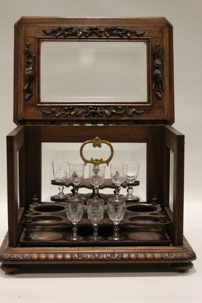Mid 1800s Walnut Liqueur Tantalus Case: Heavily carved, beveled glass, liqueur tray is completely removeable, tray should hold 4 bottles and 14 cordials, front lifts up and reveals the interior, probably black forest, 14 L 10 W 12 H