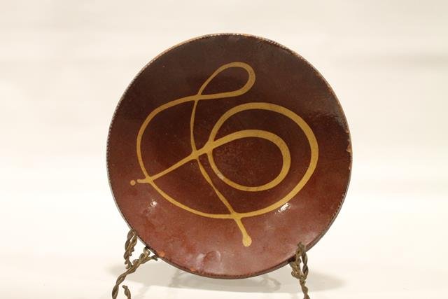 Redware Pennsylvania Pie Plate: Early 1800s redware pie plate, coggle edging, Pennsylvania, interior of yellow slip swirl decoration similar to musical staff symbol, shiny, clear lead-glazed surface, 9 1/2" across.