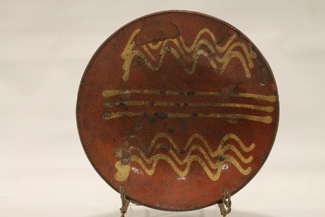 Pennsylvania Redware 11" Pie Plate: Redware pie plate, coggle edging, Pennsylvania, interior with two squiggle, three rows each on sides, center with straight line rows of yellow slip decoration, shiny, clear lead-glazed surface, 11" W.