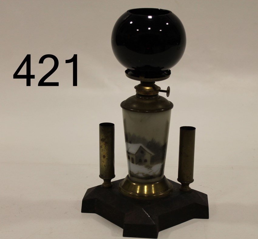 Attributed to B&H Cigar Lighting Lamp: Victorian counter top cigar lighting lamp, hand-painted Wave Crest-like lamp base of winter homestead scene, ruby red shade, 2 brass wick holders, cast iron base, attributed to B&H. 9 1/2" H.