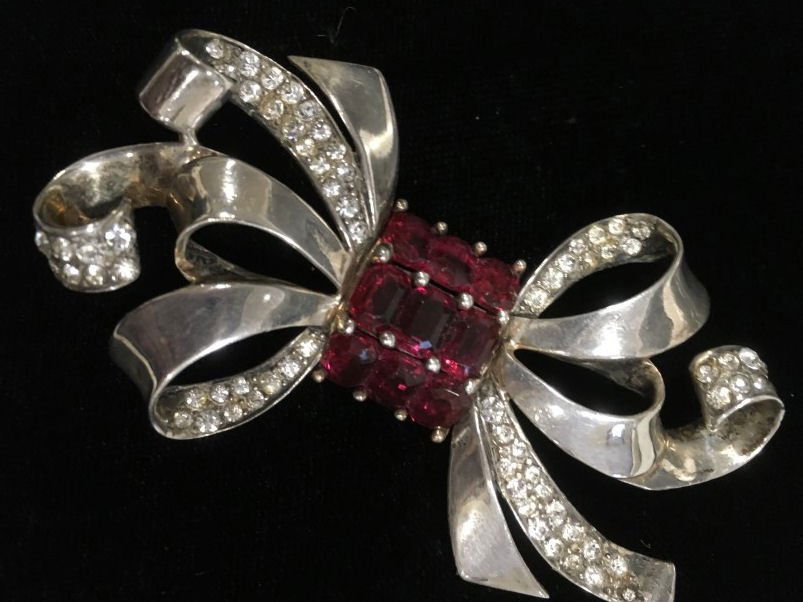 Sterling Phrygian Marcel Boucher Brooch: Marcel Boucher classic flowing bow brooch in sterling with clear and port wine-colored sets. Back bears his mid-century Phrygian mark. 3" x 1 3/4".