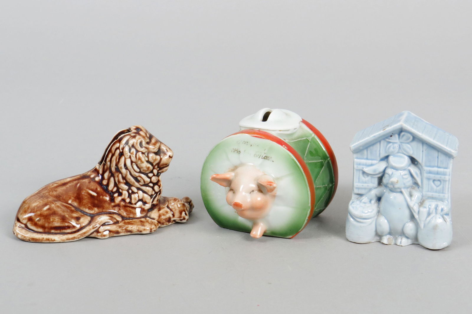 Lot of 3 Ceramic Animal Banks: 3 Animal Banks, Ceramic: Reclining Lion, Head repaired; Pig in Drum, Minor chips; Pig w/Pipe Guarding Money Sacks, Minor chips