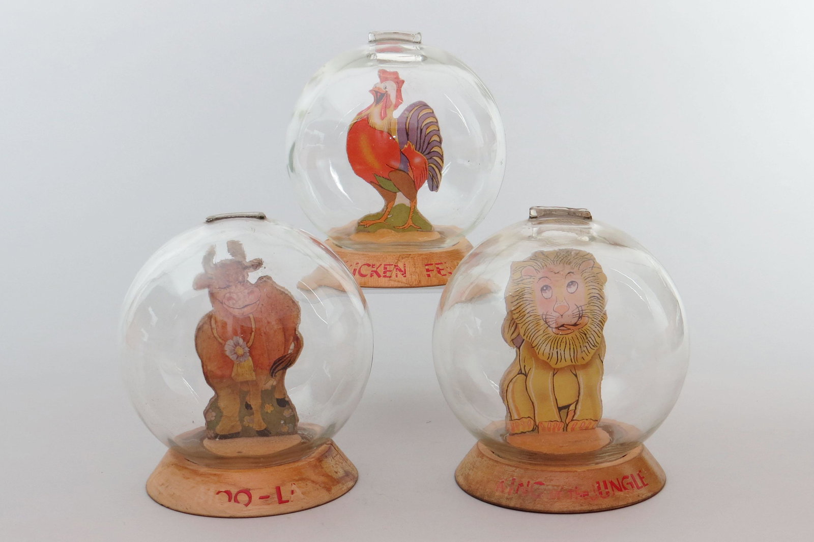 Lot of 3 Wood/Glass Bubble Banks: 3 Bubble Banks, Wood/Glass: "Moo-La", No label, partial letters; "Chicken Feed", Partial label, partial letters; "King of the Jingle", One side of insert is faded