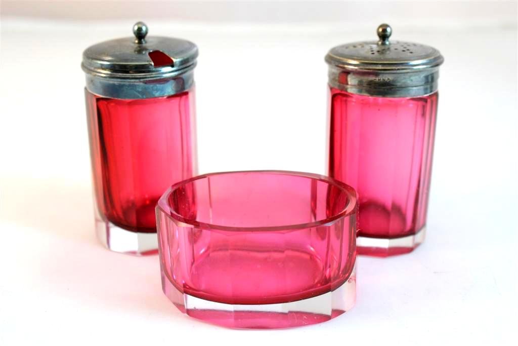 Cased Cut Glass Cranberry Condiment Set: A beautiful Antique Victorian period Cut Glass Condiment set. Made in Cranberry Cased Glass. Faceted cut. Comes with a open master salst cellar, a pepper shaker & a Condiment jar. Topped with silverpl
