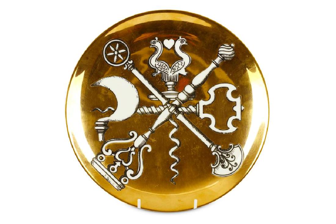 A Fornasetti porcelain cabinet plate: Pierro Fornasetti - A 1950s porcelain transfer printed cabinet or lunch plate from the 'Posateria' series, decorated with bottle openers, implements and forks to a gilded ground, diameter 25.5cm