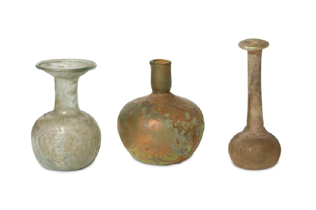 THREE ROMAN GLASS FLASKS Circa 2nd - 4th Century A.D.: THREE ROMAN GLASS FLASKS Circa 2nd - 4th Century A.D. Including a pale blue glass example with a globular ribbed body, a tall cylindrical neck and wide everted rim; a squat blue glass vessel with a sh
