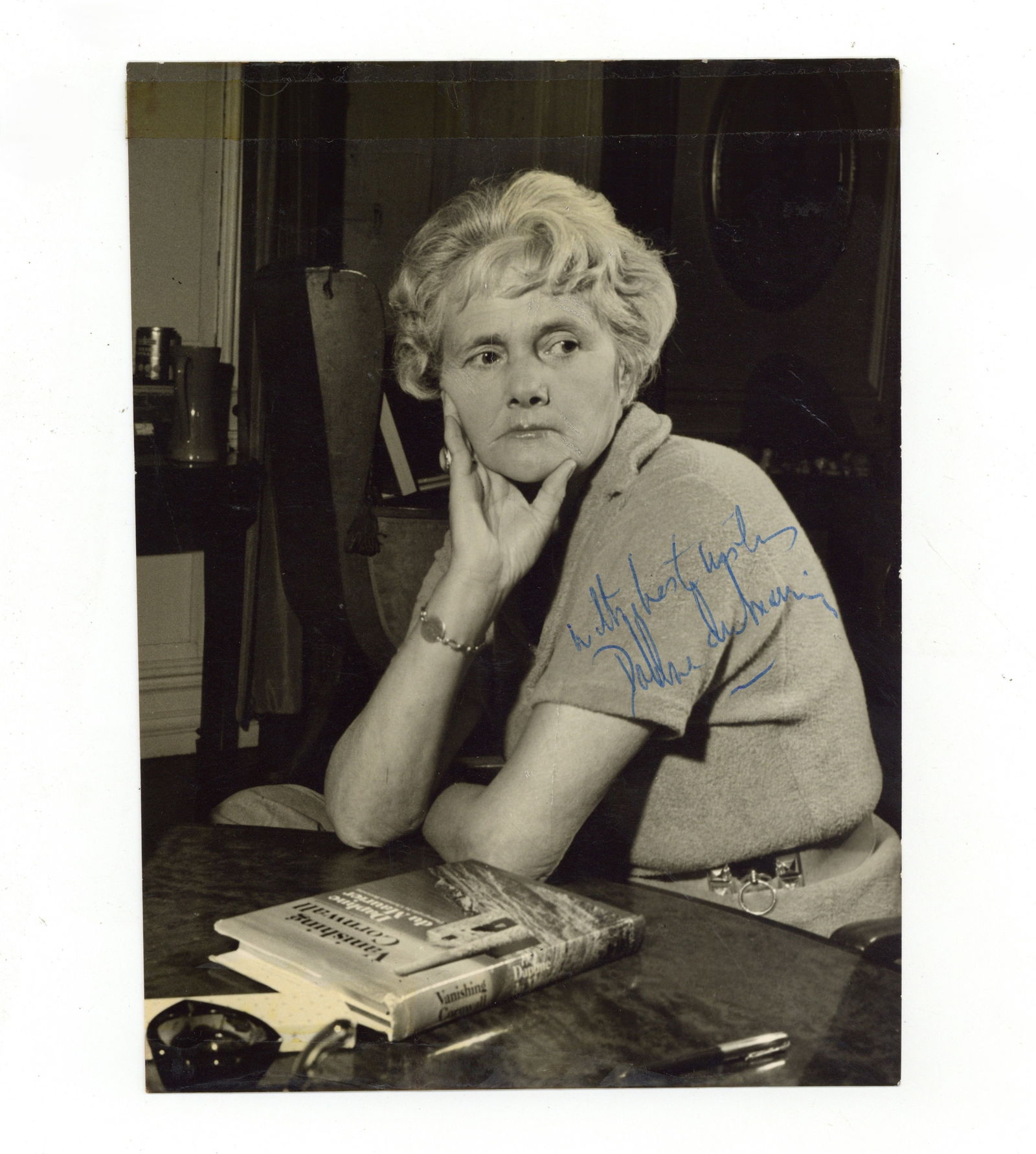 Du Maurier (Daphne) Signed photograph: Du Maurier (Daphne) Signed photograph Vintage black and white photograph of the British author at her desk, signed in blue ballpoint ink "With best wishes, Daphne du Maurier", some handling wear and