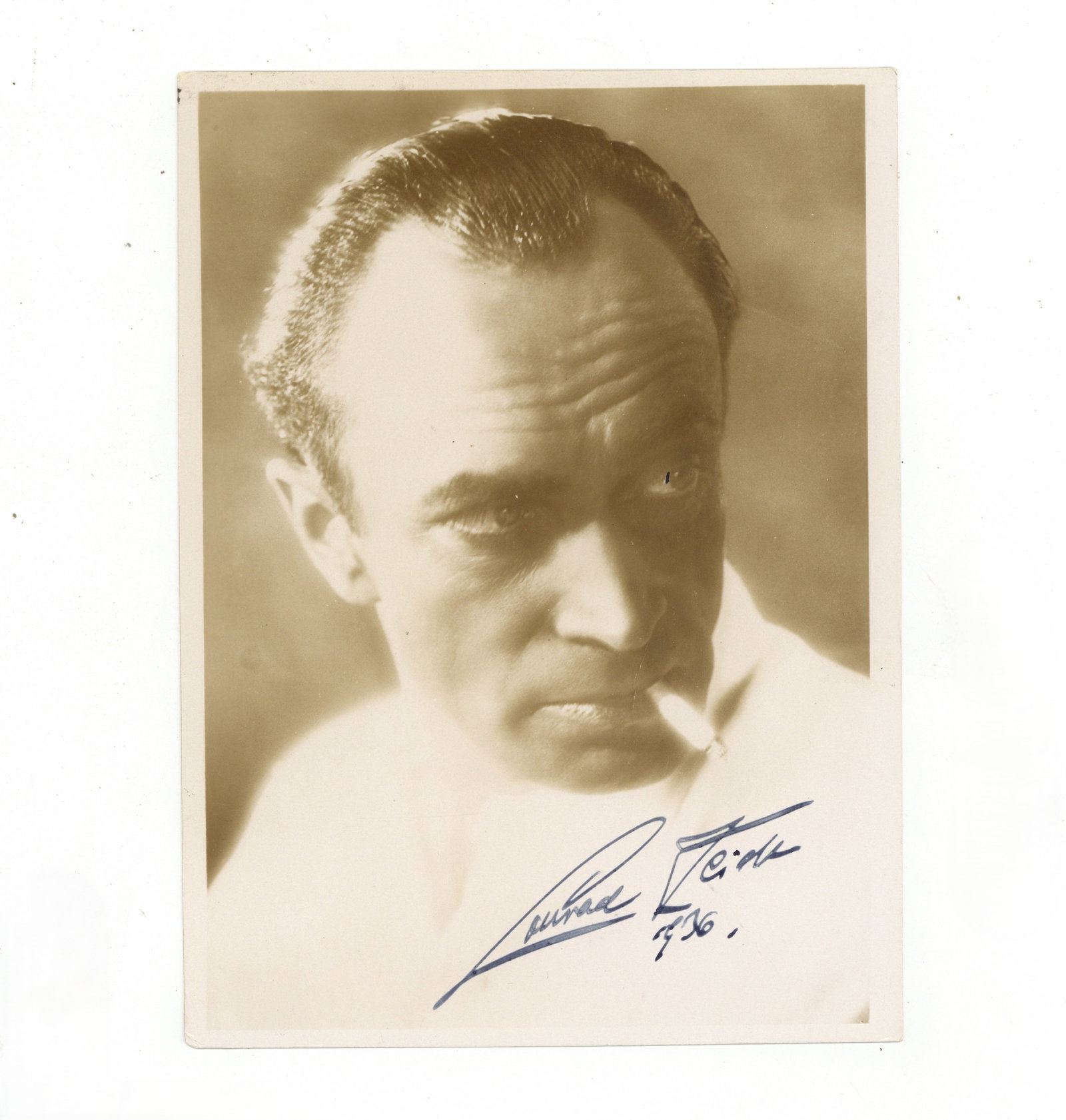 Veidt (Conrad) Signed photograph: Veidt (Conrad) Signed photograph Vintage photograph of Veidt smoking a cigarette, signed in fountain pen, “Conrad Veidt, 1936", light handling wear. Dimensions:7 x 5"/ 18 x 12cm