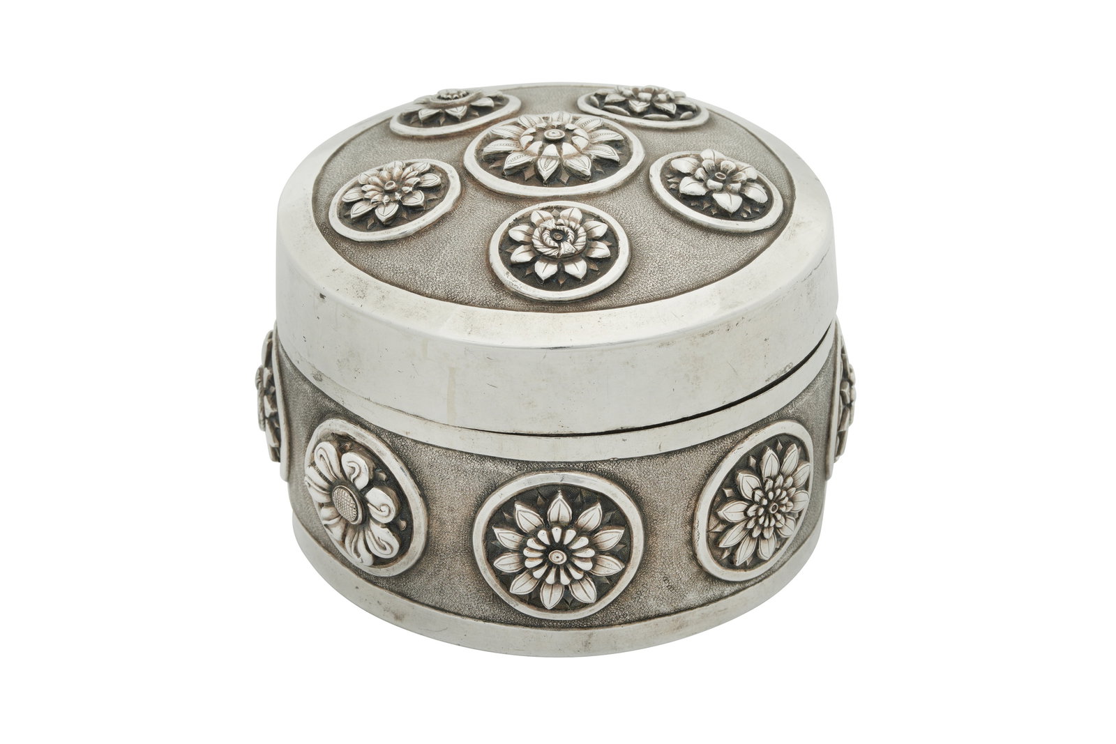 Deccan circa 1890 A late 19th century Anglo - Indian unmarked silver box: Raj period, of cylindrical form with a domed pull off lid. The base with eight circular vignettes finely chased with an individual flower head to each, all against a textured ground. The lid similarit