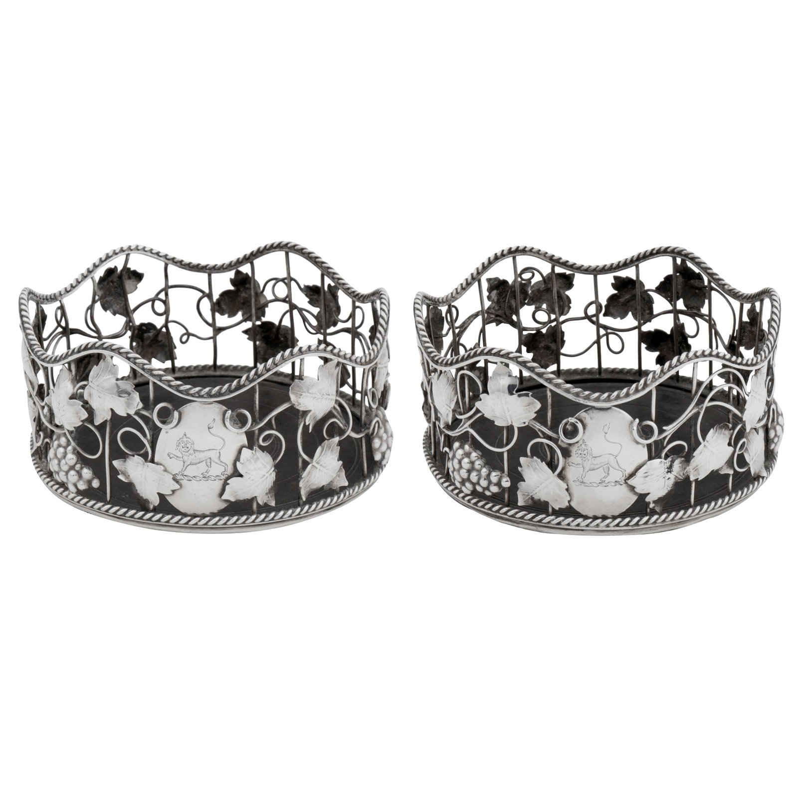London 1767 by William Plumber A pair of George III sterling silver wine coasters: Each of circular form with wavy beaded rims, the wirework sides with applied fruiting vine, an oval cartouche engraved with a contemporaneous crest of a lion passant regardant. Inset ebony bases. Each
