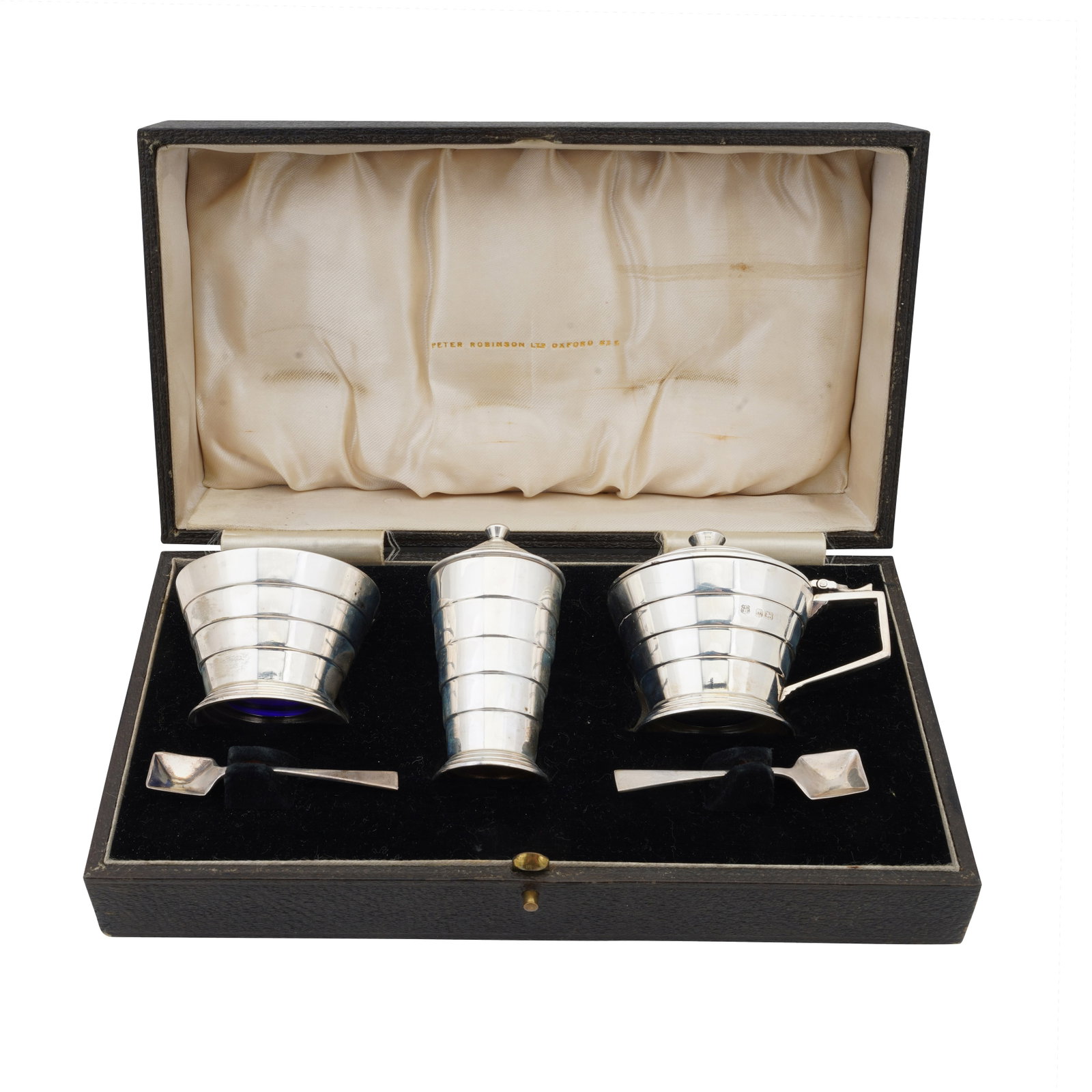 Birmingham 1935 by Barker Brothers Silver Ltd A cased George V Art Deco sterling silver three-piece: Birmingham 1935 by Barker Brothers Silver Ltd A cased George V Art Deco sterling silver three-piece cruet set Comprising a mustard pot, a pepper, and a salt, replete with spoons. Weight – 113